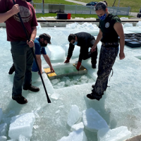 People standing on ice with a square cut into the ice.