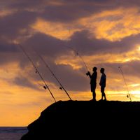 Two people with fishing poles on a shoreline.