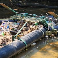 A trash trap device installed in a river that has captured plastic bottles and other marine debris to prevent it from traveling to other areas.