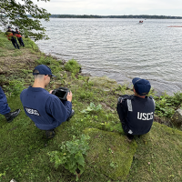 Uniformed individual pilots a drone from a bank of a water body during training exercise.