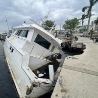 A half sunken abandoned derelict vessel that crashed into a marina walkway marked off with caution tape.