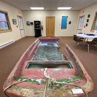 A broken boat staged in the center of a room within an aquarium.