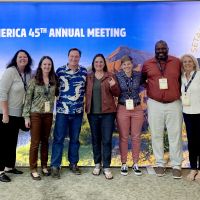 Individuals stand in a group and smile in front of an Society of Environmental Toxicology and Chemistry-themed backdrop.