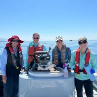 Four research team members smile for a group photo aboard a research vessel.