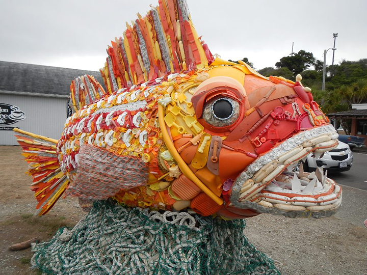 A large, bright orange fish sculpture made from ocean trash, mostly plastic.